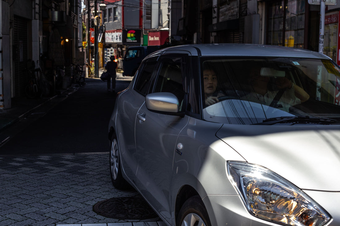 高架下を抜けてくる乗用車、運転する女性